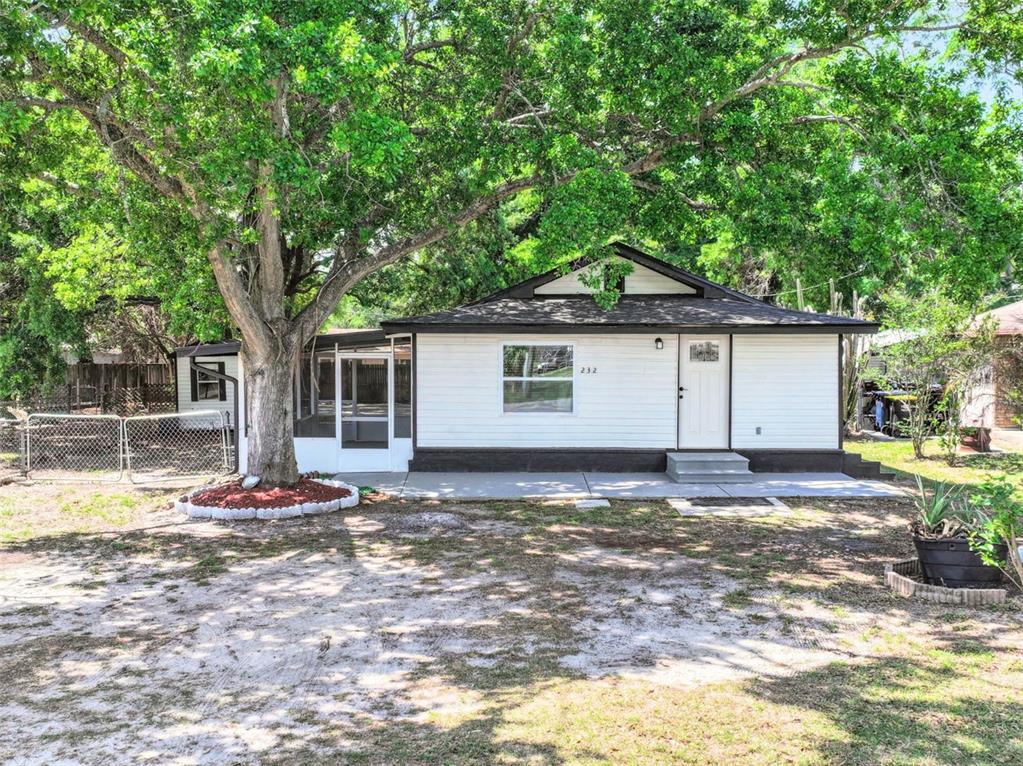 A white single-story house with a dark roof, a front porch, and a large tree — 232 NOXON STREET, AUBURNDALE, FL
