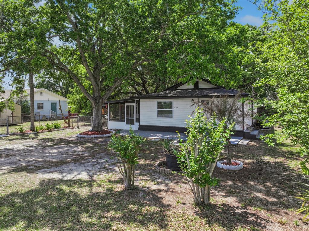 A white single-story house with a screened porch sits on a grassy lot with trees — 232 NOXON STREET, AUBURNDALE, FL