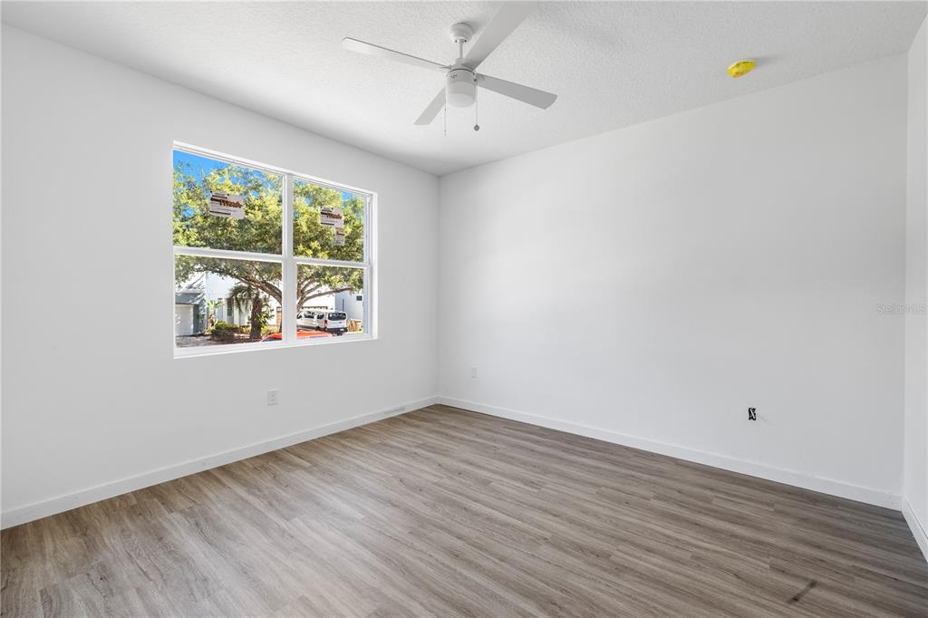 An empty bedroom with white walls, wood-look flooring, a ceiling fan, and a large window — 7511 NORTHERN HARRIER WAY UNIT 102, KISSIMMEE, FL
