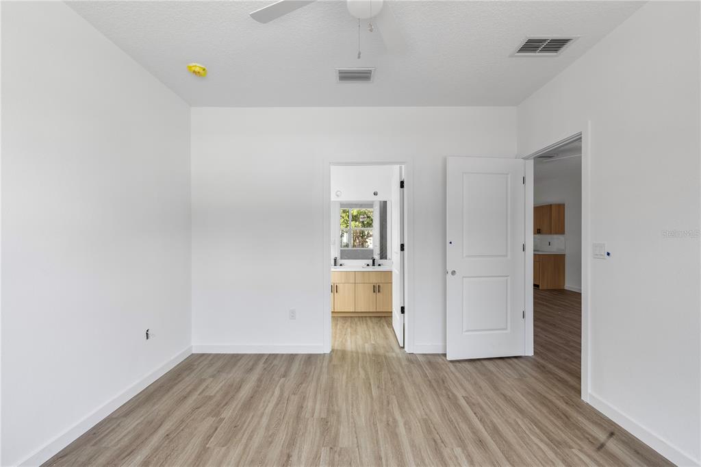 A bedroom with light wood-look flooring, white walls, and an open doorway to a bathroom — 7511 NORTHERN HARRIER WAY UNIT 102, KISSIMMEE, FL