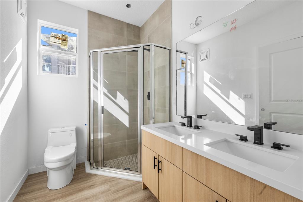 A modern bathroom features a double vanity, a glass-enclosed shower, and a white toilet — 7511 NORTHERN HARRIER WAY UNIT 102, KISSIMMEE, FL