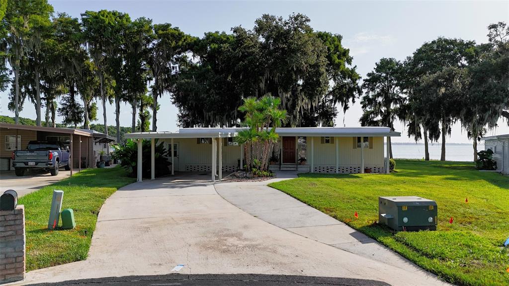 A single-story house with a carport and a large yard sits near a lake — 34410 ISLAND DRIVE, LEESBURG, FL