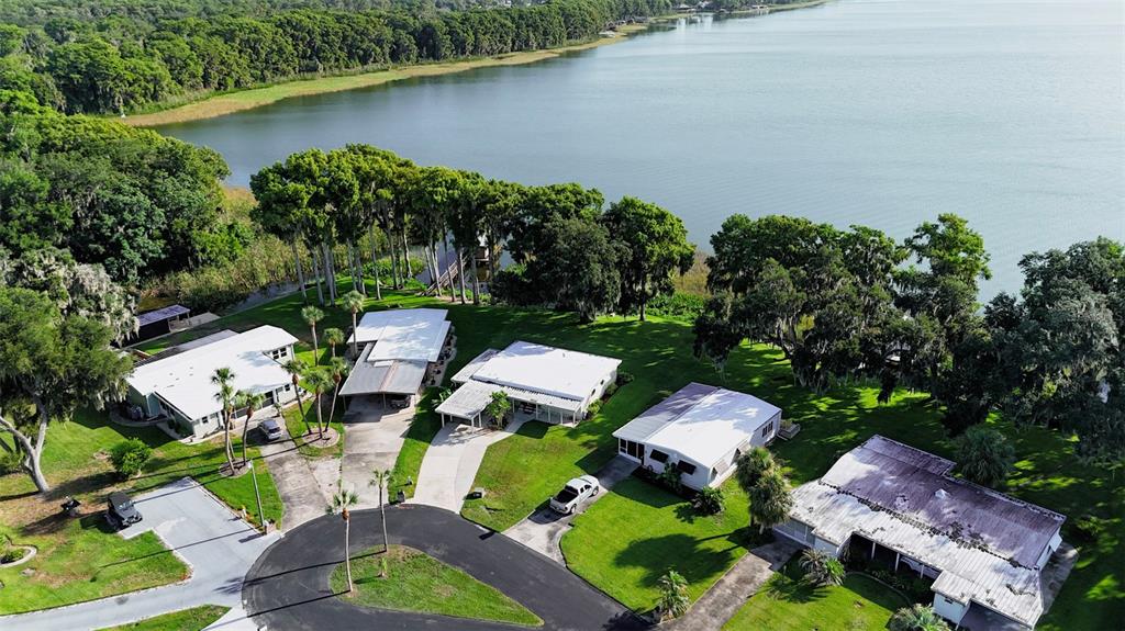 An aerial view shows several single-story houses with white roofs situated along a lakefront — 34410 ISLAND DRIVE, LEESBURG, FL