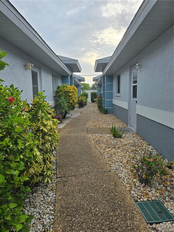 A narrow concrete walkway leads between two light blue residential buildings with gravel landscaping — 6551 HAMLET DRIVE UNIT B, ENGLEWOOD, FL