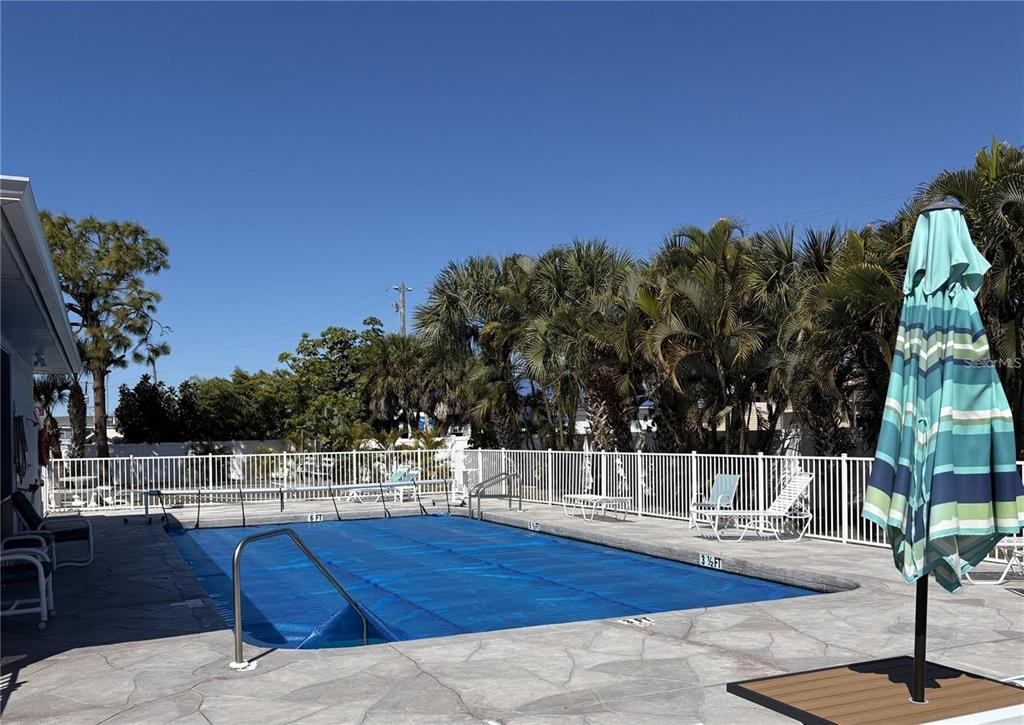 A rectangular swimming pool with a blue cover is surrounded by a patio and palm trees — 6551 HAMLET DRIVE UNIT B, ENGLEWOOD, FL
