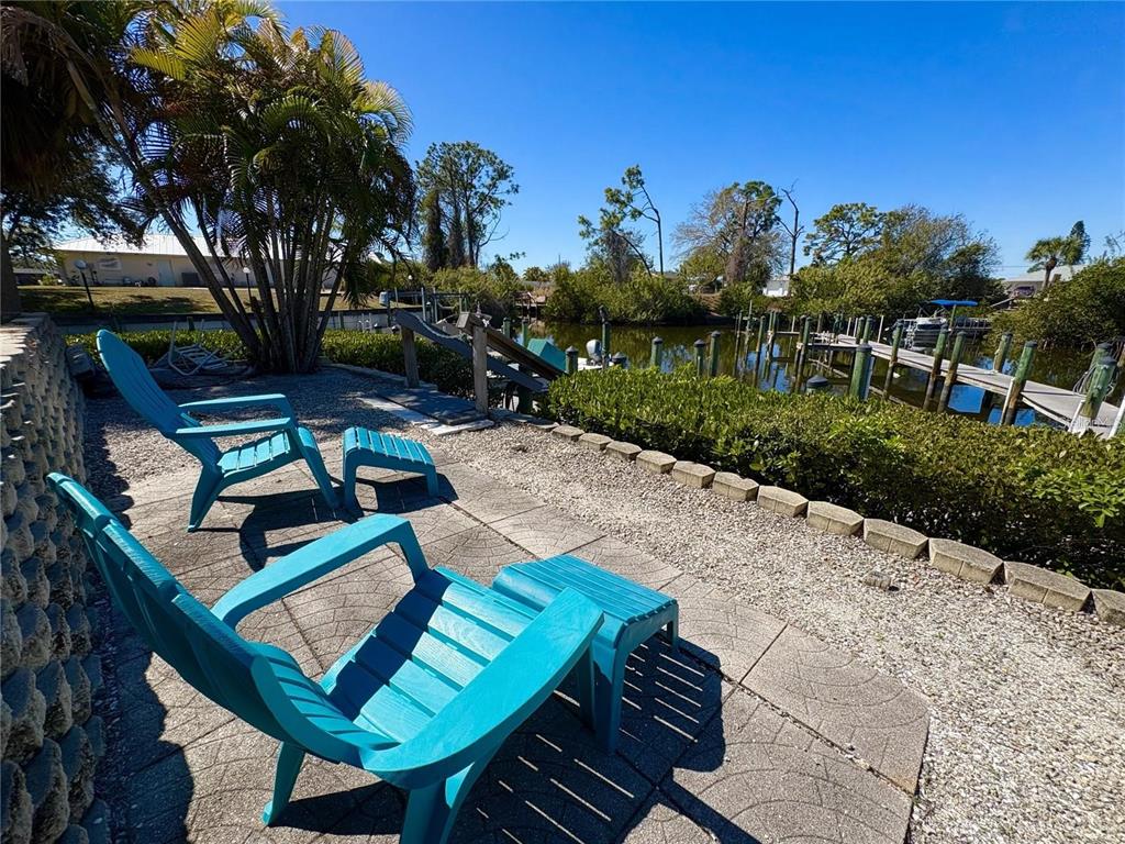 Two blue Adirondack chairs with matching ottomans sit on a patio overlooking a canal — 6551 HAMLET DRIVE UNIT B, ENGLEWOOD, FL