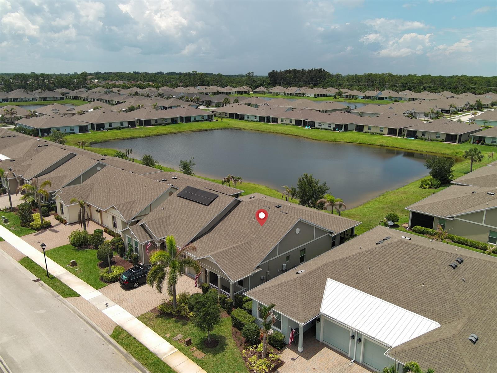 An aerial view shows a residential neighborhood with houses surrounding a central pond — 5932 Spicewood Lane, Vero Beach FL 32966, VERO BEACH, FL