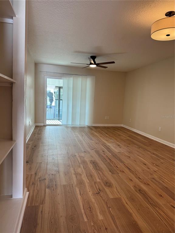 An empty living room features wood-look flooring, a ceiling fan, and a sliding glass door — 3819 N OAK DRIVE UNIT I42, TAMPA, FL