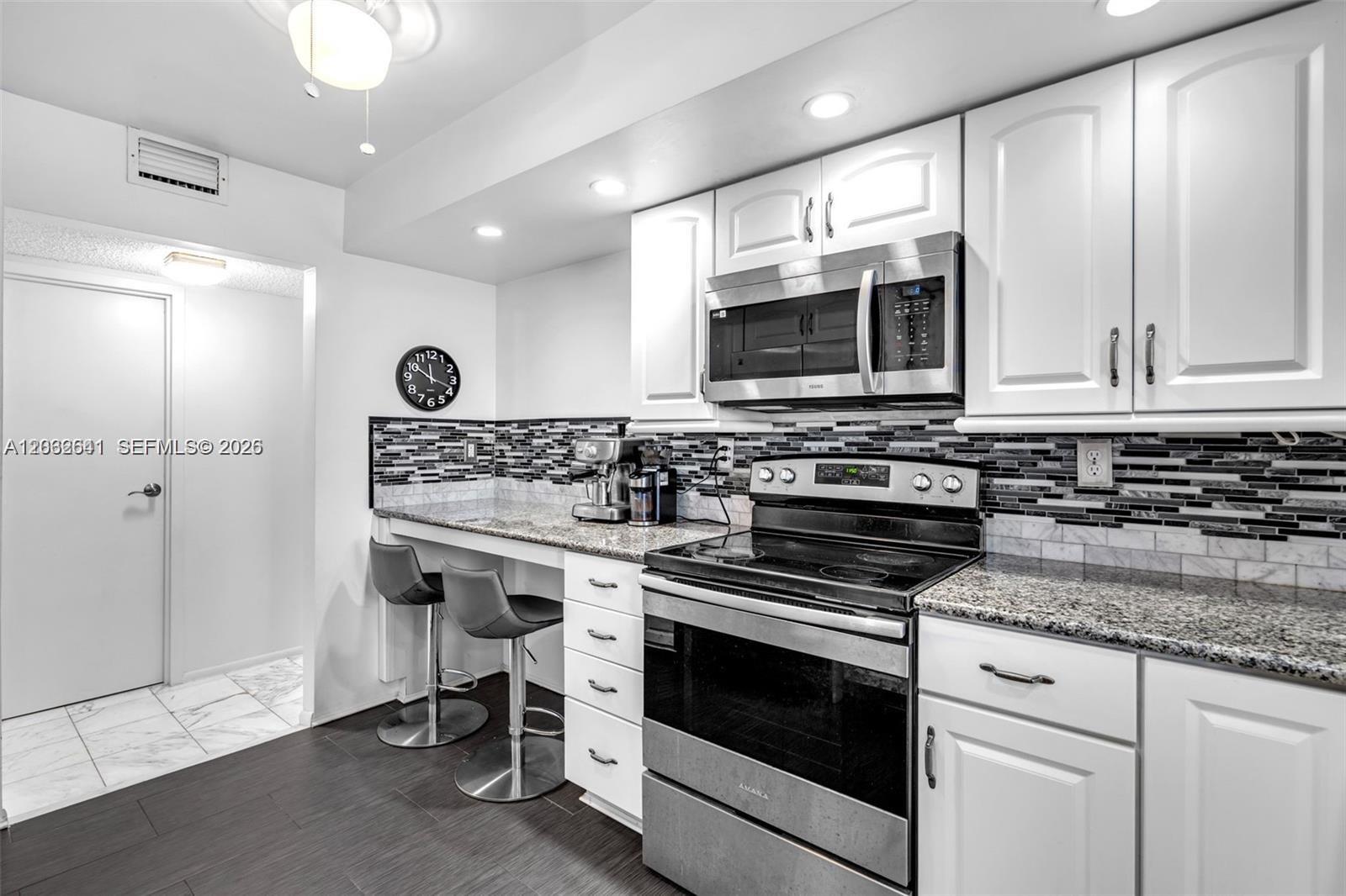 A modern kitchen features white cabinets, stainless steel appliances, granite countertops, and a breakfast bar — 1000 Parkview Dr # 715, Hallandale Beach FL 33009, HALLANDALE BEACH, FL
