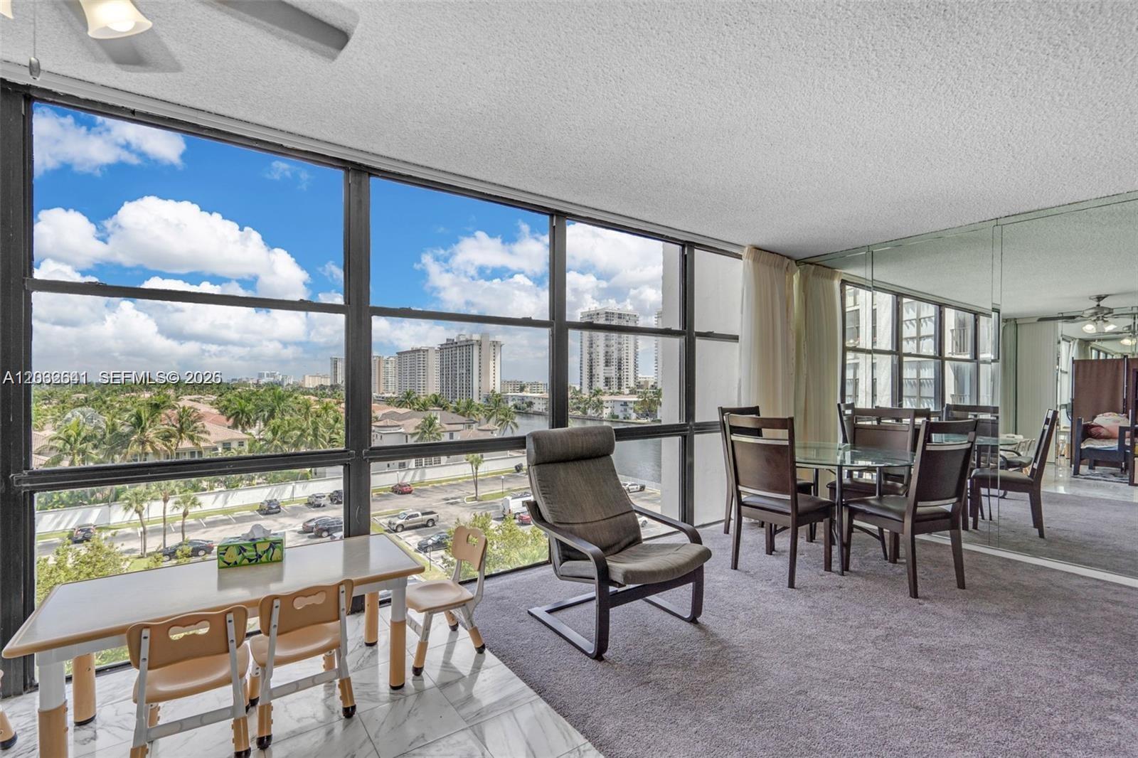 A dining area with a glass table, carpeted flooring, and large windows overlooking a city — 1000 Parkview Dr # 715, Hallandale Beach FL 33009, HALLANDALE BEACH, FL