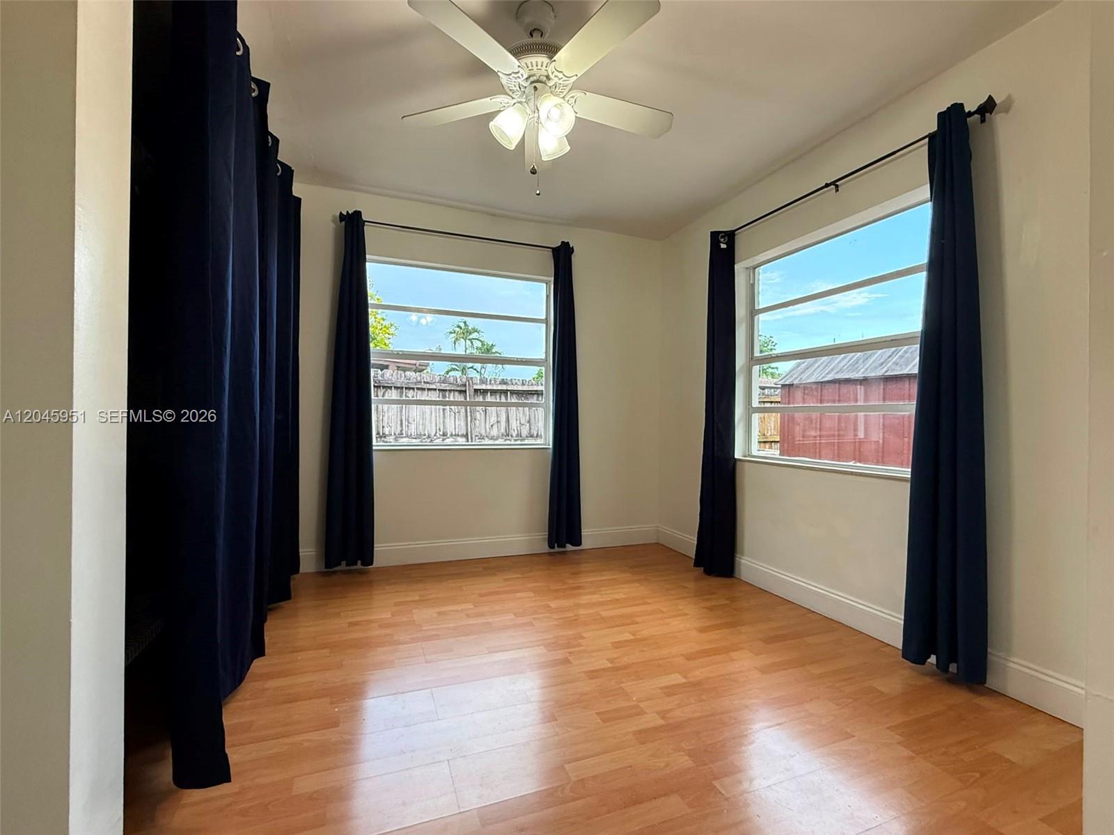 An empty room features light wood flooring, a ceiling fan, and dark curtains on windows — 13330 SW 79th St, Miami FL 33183, MIAMI, FL