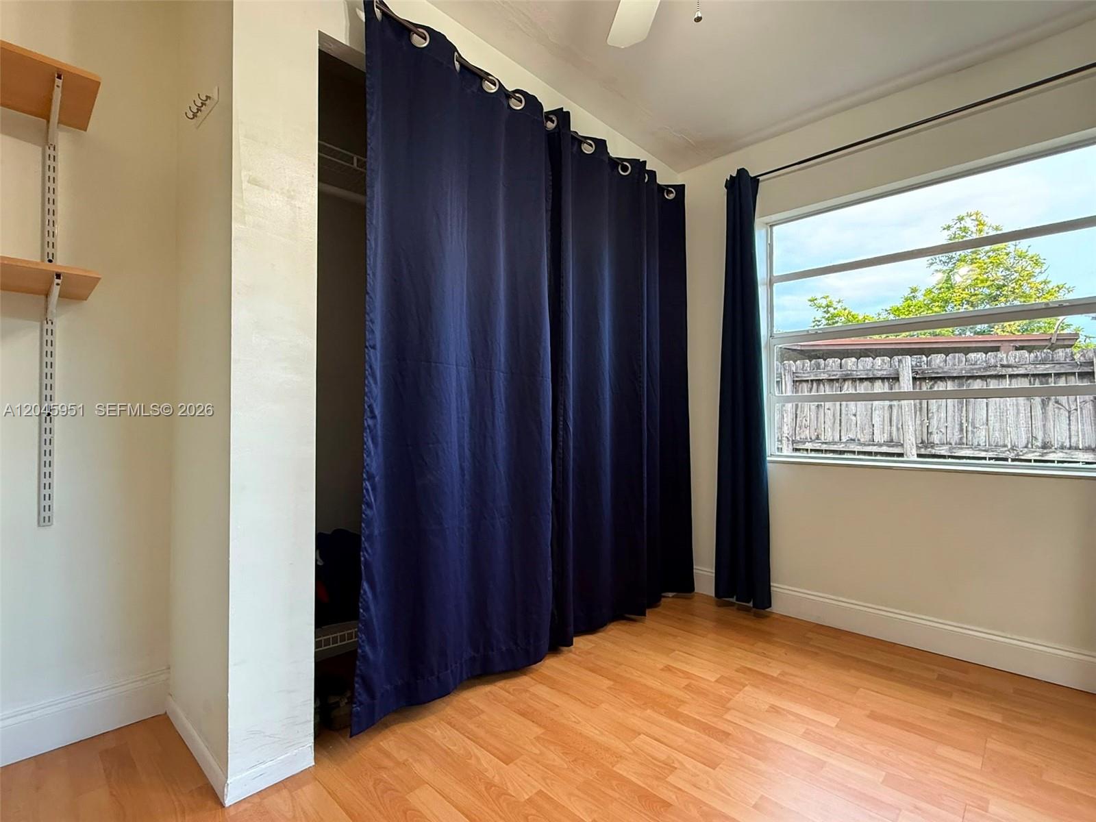 A bedroom features light wood flooring, a closet with navy curtains, and a window view — 13330 SW 79th St, Miami FL 33183, MIAMI, FL
