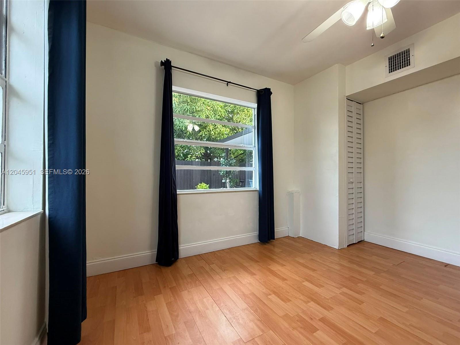 An empty bedroom features light wood-look flooring, white walls, dark curtains, and a closet — 13330 SW 79th St, Miami FL 33183, MIAMI, FL