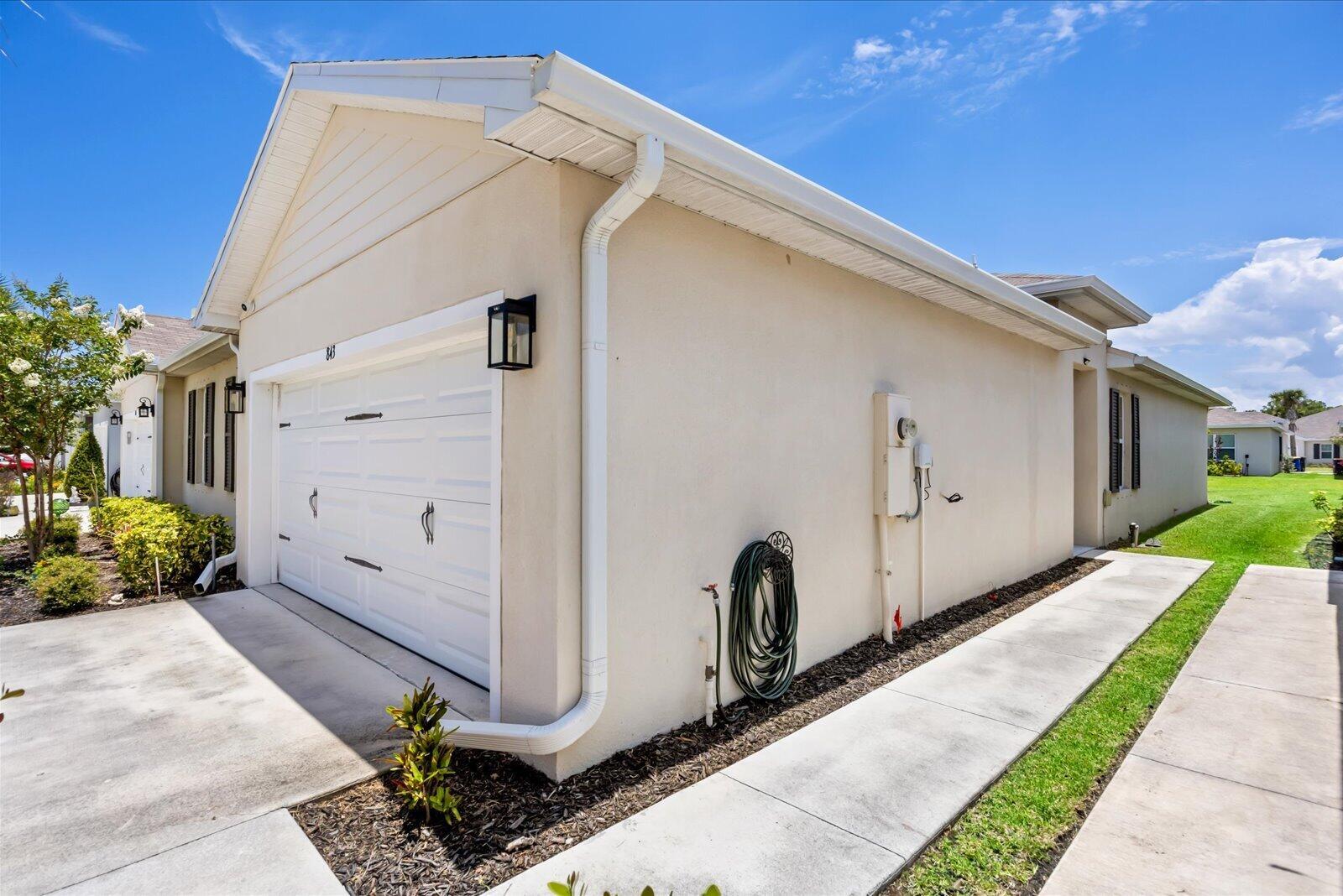 The exterior of a beige house features a white garage door, downspout, and concrete walkway — 843 Persimmon Place, Fort Pierce FL 34981, FORT PIERCE, FL