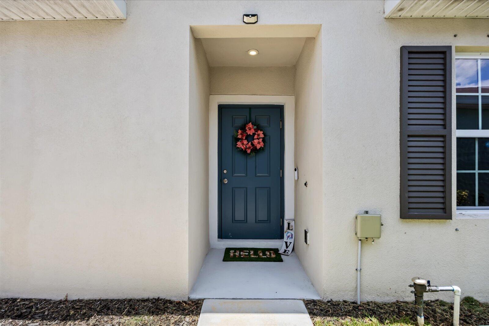 A blue front door with a wreath and a welcome mat sits in a recessed entryway — 843 Persimmon Place, Fort Pierce FL 34981, FORT PIERCE, FL