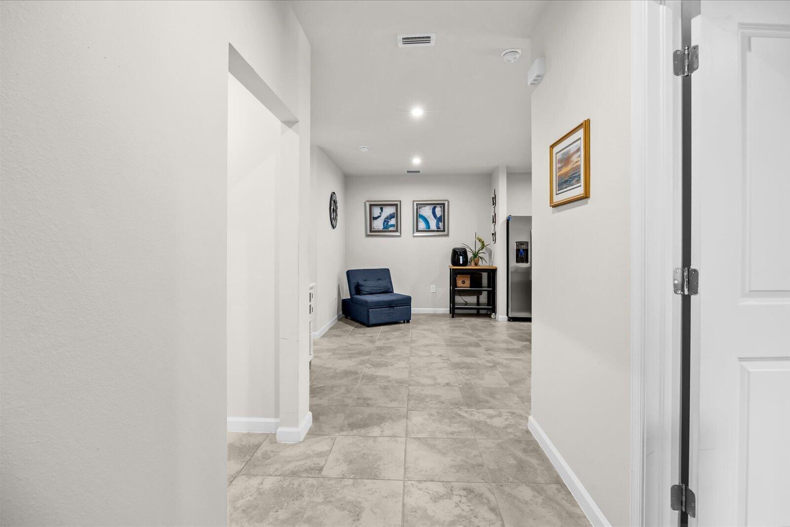 A hallway leads to an open area with tile flooring, a blue chair, and artwork — 843 Persimmon Place, Fort Pierce FL 34981, FORT PIERCE, FL