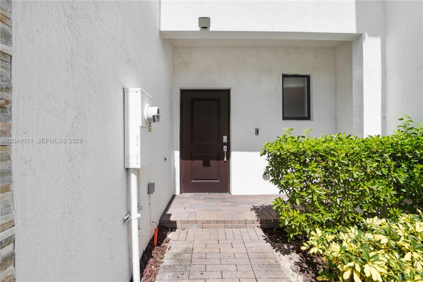A brown front door is set in a white stucco wall with a brick walkway — 20610 NE 5th Pl, Miami FL 33179, MIAMI, FL