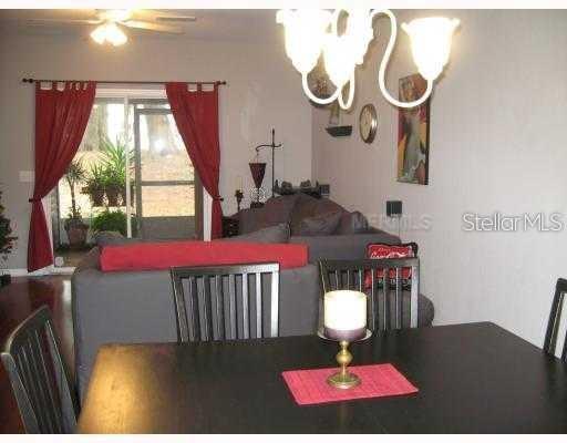 A dining table with a candle centerpiece sits before a living room with red curtains — 4169 PLANTATION COVE DRIVE, ORLANDO, FL