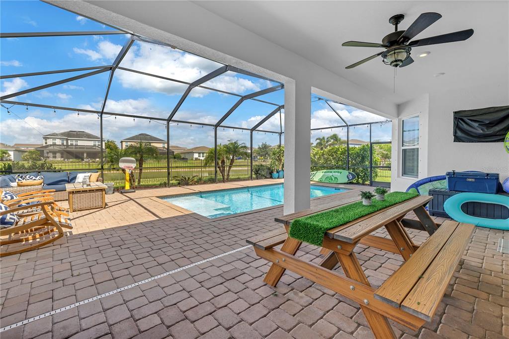 A covered patio features a picnic table, pool, and screened enclosure overlooking a pond — 10108 CORRIENTE COURT, PALMETTO, FL