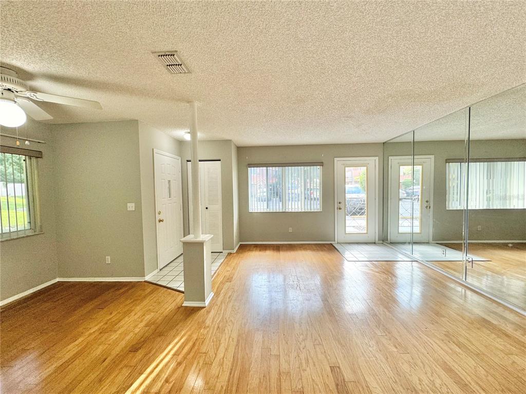 A living room with hardwood floors, a mirrored wall, a ceiling fan, and an entryway — 8302 WATERVIEW WAY UNIT 8302, WINTER HAVEN, FL