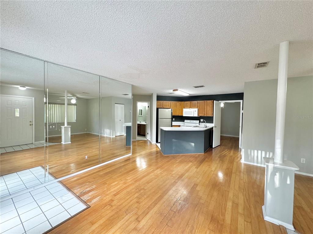 A living room with hardwood floors, mirrored walls, and an open kitchen with dark cabinetry — 8302 WATERVIEW WAY UNIT 8302, WINTER HAVEN, FL