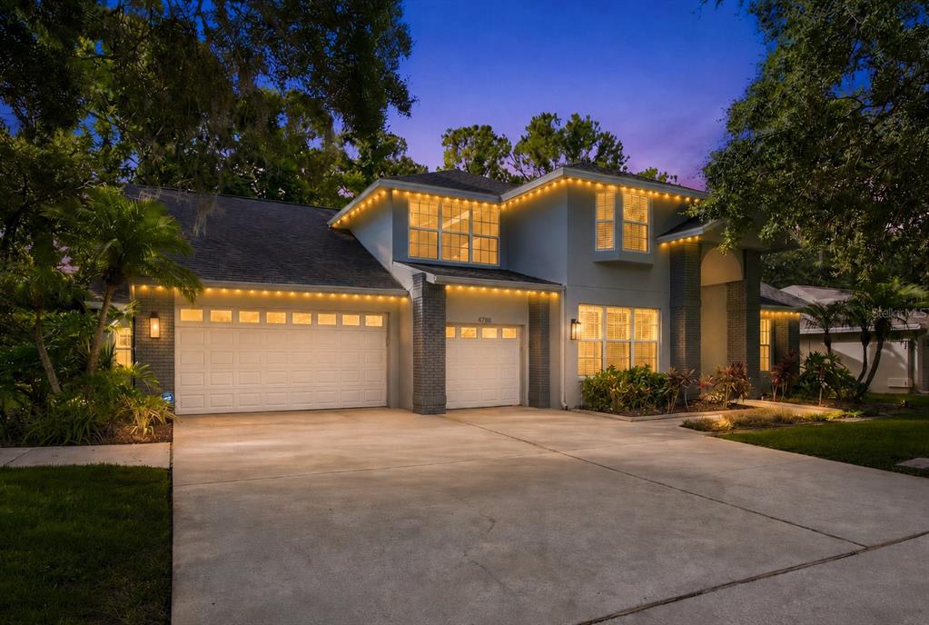 A two-story house with a two-car garage and exterior holiday lighting at dusk — 4788 BRAYTON TERRACE S, PALM HARBOR, FL