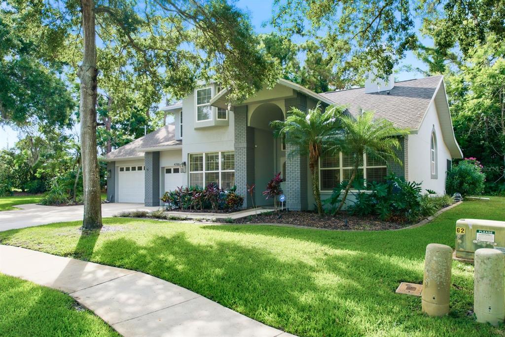 A two-story suburban house with a gray brick facade, a two-car garage, and mature trees — 4788 BRAYTON TERRACE S, PALM HARBOR, FL