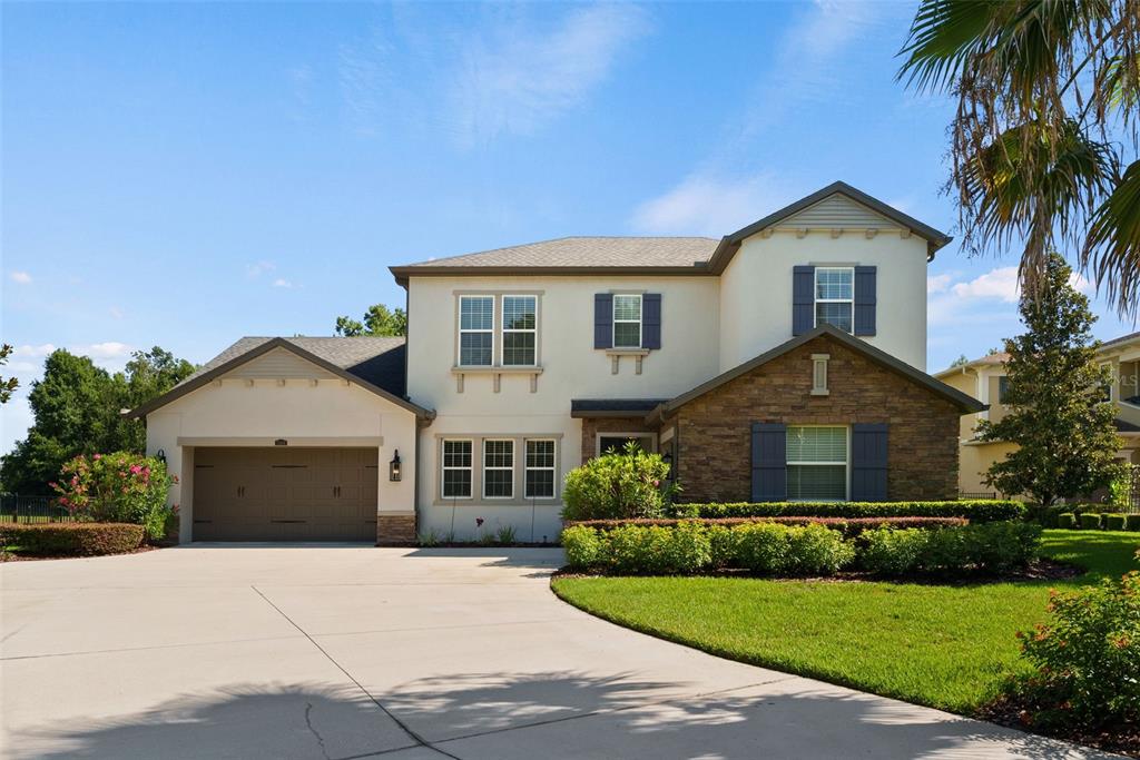 A two-story suburban house with a stone facade, garage, and a large concrete driveway — 2608 MEADOW GRANGE LANE, LUTZ, FL
