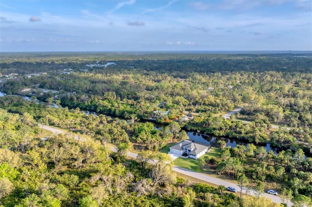 An aerial view shows a house situated next to a canal surrounded by dense forest — 14351 HOWARD AVE, PORT CHARLOTTE, FL