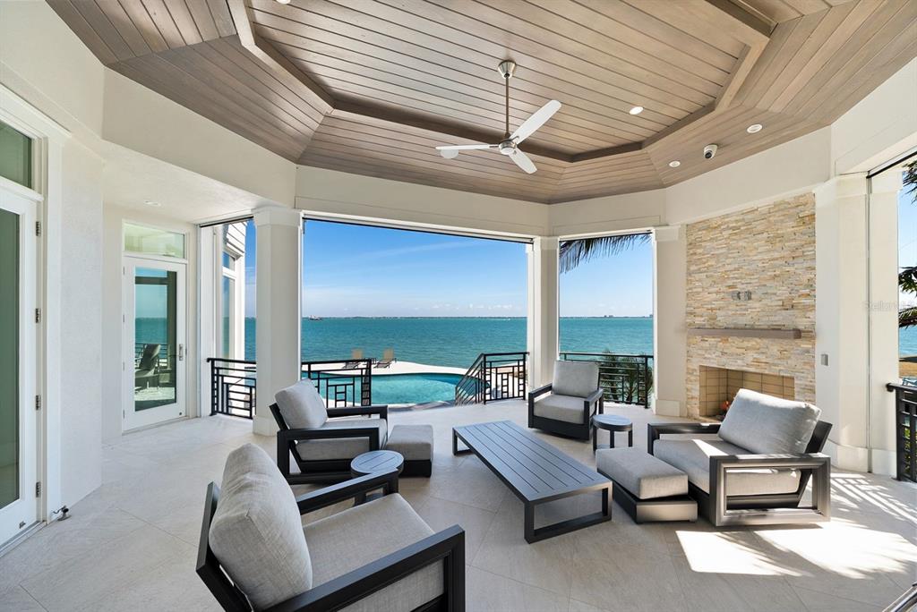 A covered outdoor patio features a stone fireplace, seating area, and views of the ocean — 600 PUTTER LANE, LONGBOAT KEY, FL