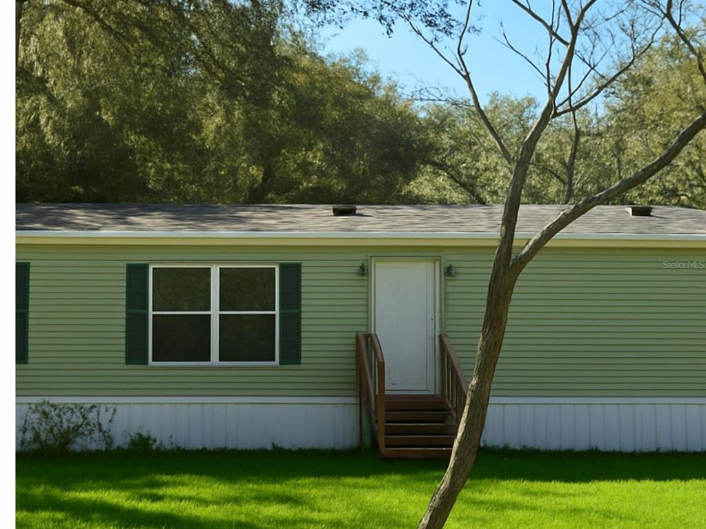 A light green mobile home features a white door, a window with shutters, and wooden steps — 14640 NE 149TH LANE, FORT MC COY, FL