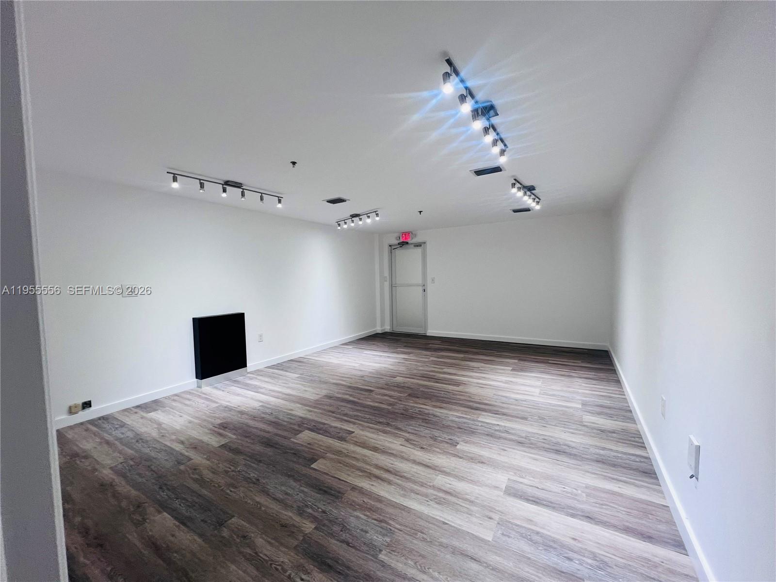 An empty room features white walls, wood-look flooring, and multiple track lighting fixtures on the ceiling — 7500 NW 25th St # 256, Miami FL 33122, MIAMI, FL