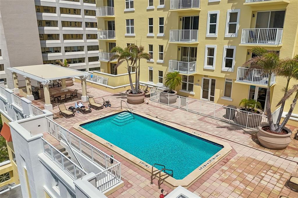 An elevated view of a swimming pool and patio area at a yellow apartment building — 628 CLEVELAND STREET UNIT 904, CLEARWATER, FL