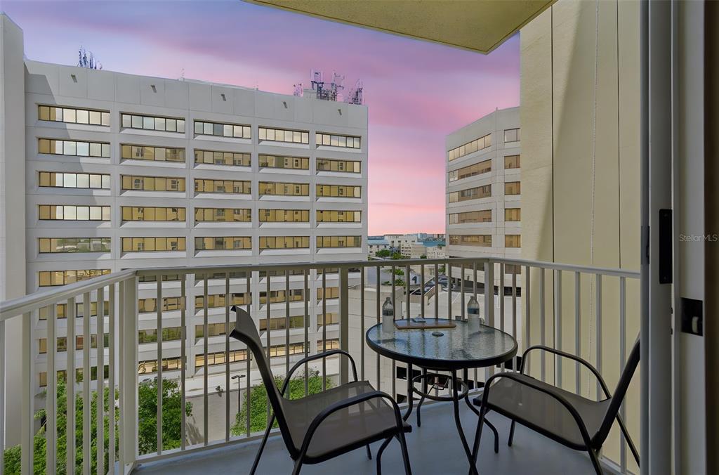 A balcony with a small table and two chairs overlooks a large office building — 628 CLEVELAND STREET UNIT 904, CLEARWATER, FL