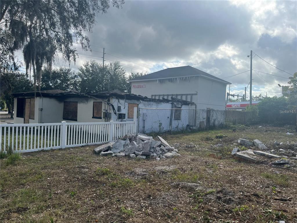 A fire-damaged building with boarded windows stands behind a white fence and debris pile — 2111 E 93RD AVENUE, TAMPA, FL