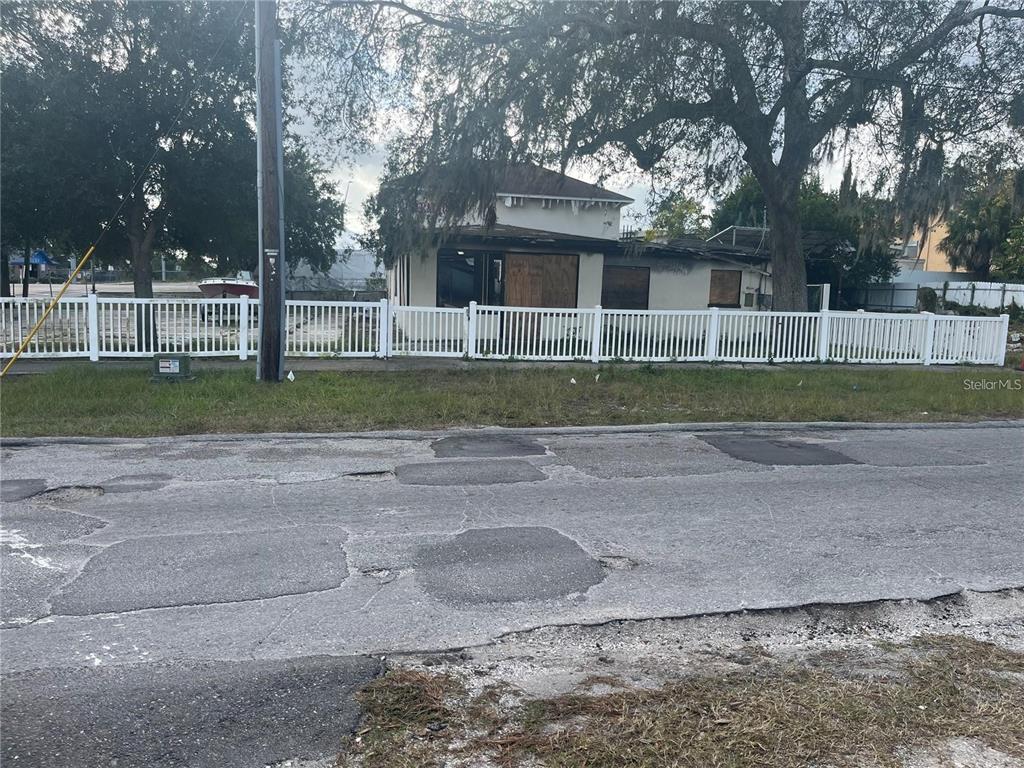A single-story house with boarded-up windows sits behind a white picket fence — 2111 E 93RD AVENUE, TAMPA, FL
