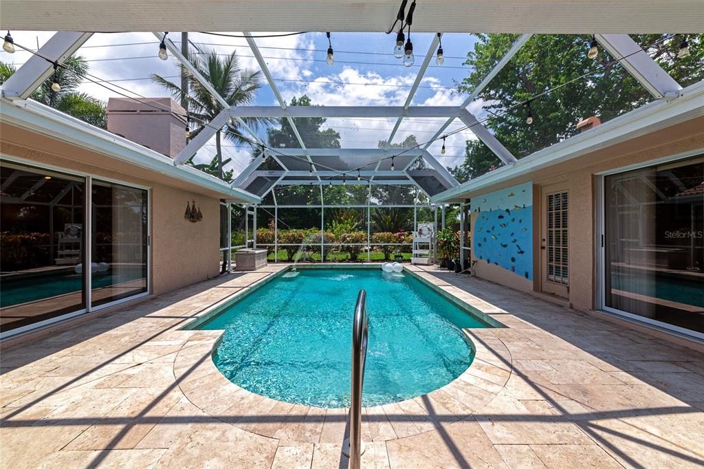 A screened-in swimming pool patio features light-colored stone decking and a painted mural wall — 1495 LANDVIEW LANE, OSPREY, FL