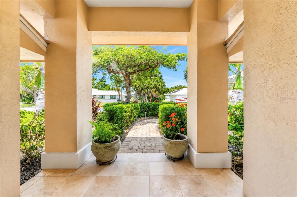 A view from a tiled covered entryway looking out toward a brick path and landscaping — 1495 LANDVIEW LANE, OSPREY, FL