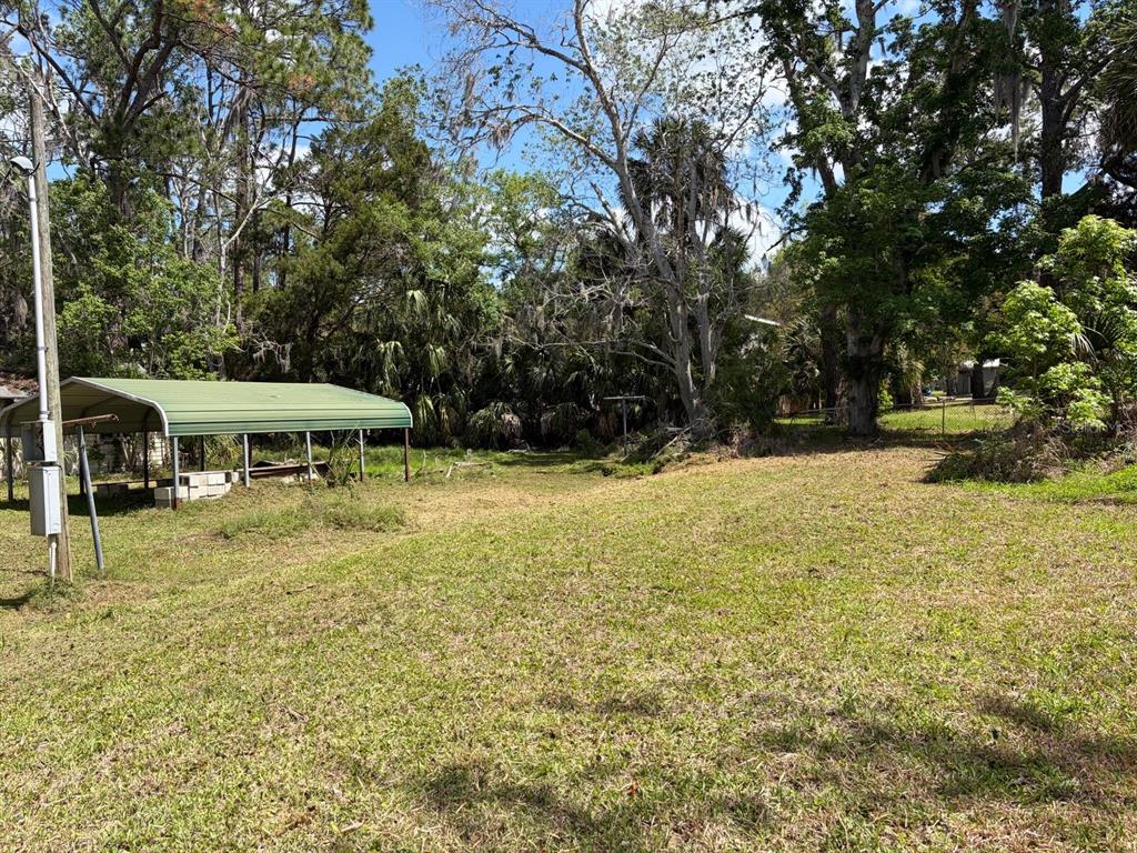A grassy lot features a green metal carport structure under a canopy of mature trees — 38 65TH STREET, YANKEETOWN, FL