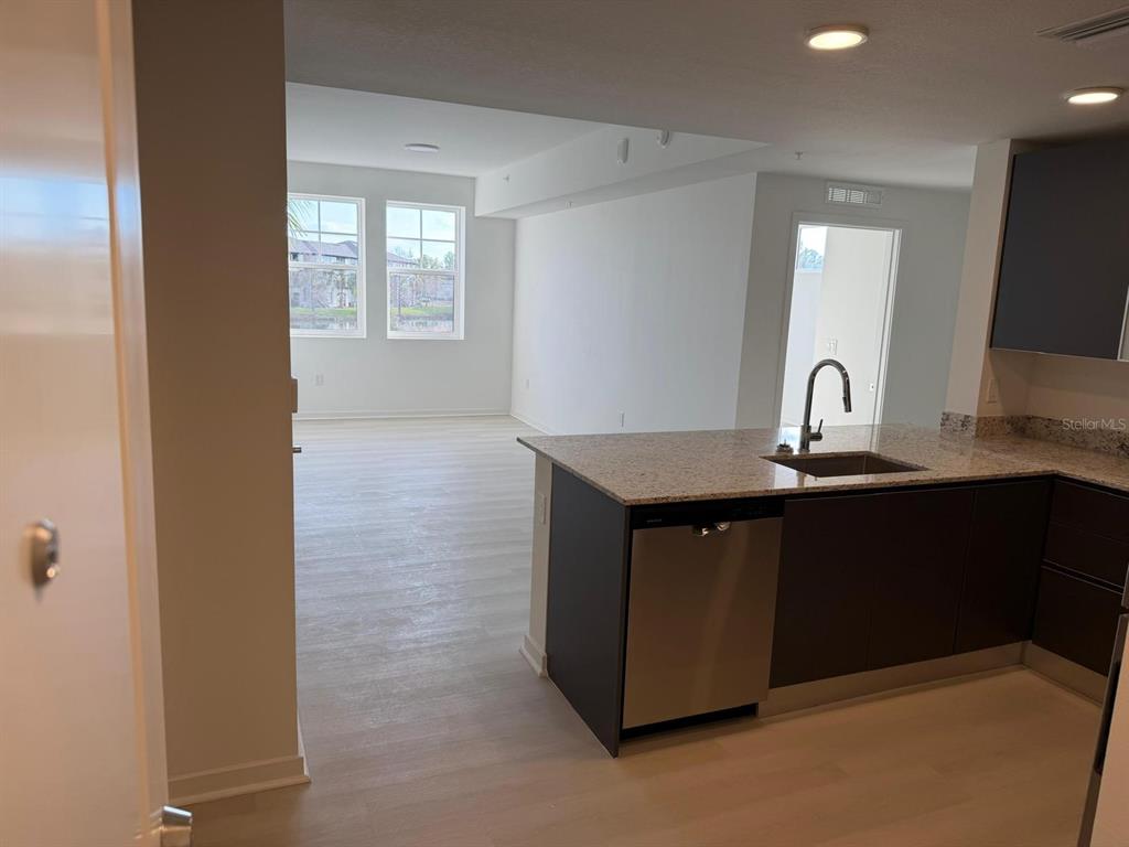 A kitchen with dark cabinets and granite countertops overlooks an open-concept living area — 5587 MILLENIA PARK BOULEVARD UNIT 222, ORLANDO, FL