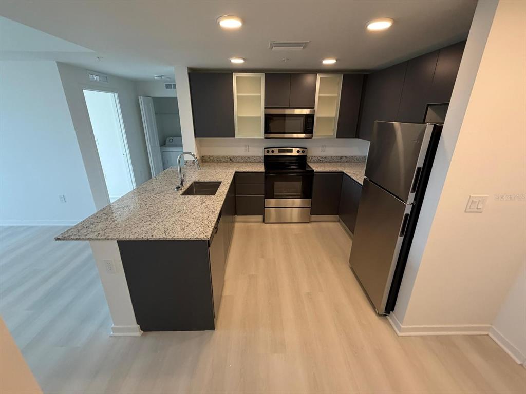 A modern kitchen features dark cabinetry, granite countertops, stainless steel appliances, and light wood flooring — 5587 MILLENIA PARK BOULEVARD UNIT 222, ORLANDO, FL