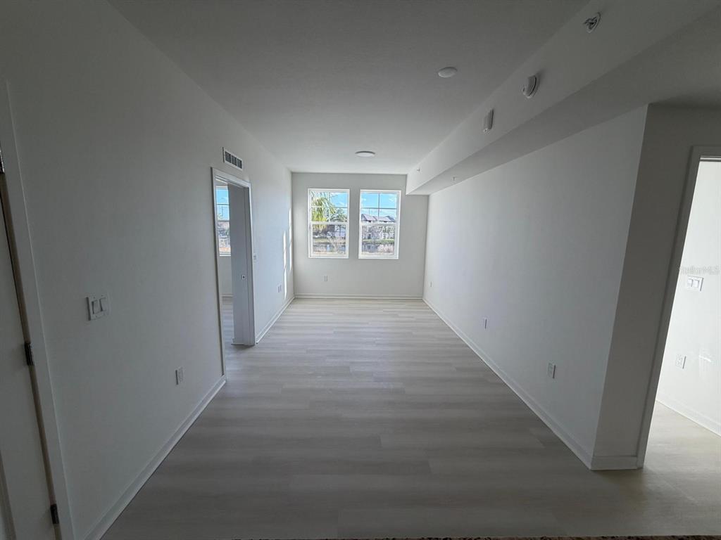 An empty room with white walls, light wood-look flooring, and two windows overlooking a pond — 5587 MILLENIA PARK BOULEVARD UNIT 222, ORLANDO, FL