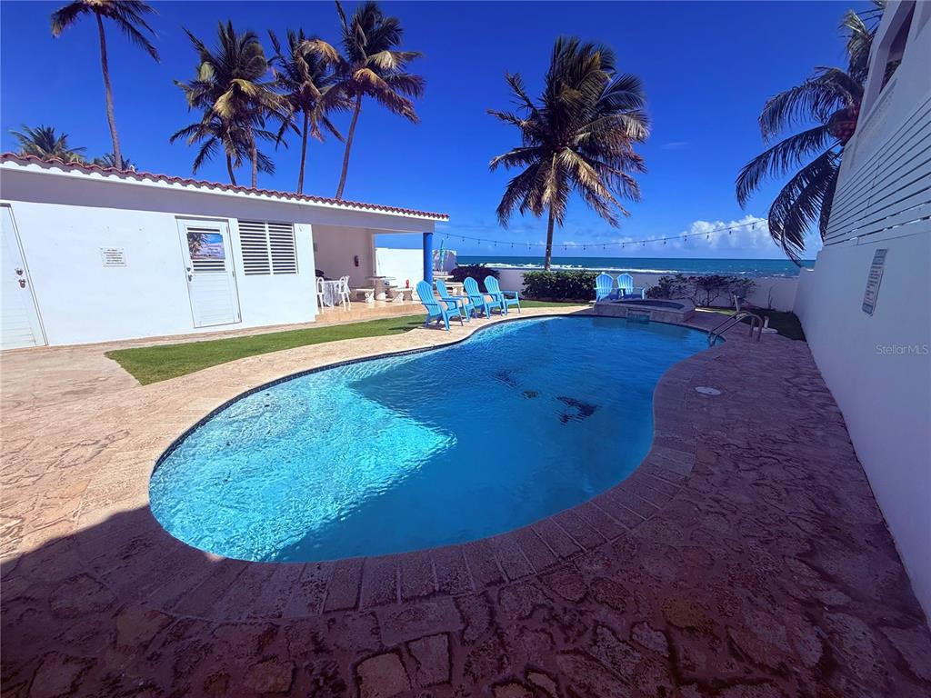 A kidney-shaped swimming pool sits on a stone patio beside a white house and ocean — Carr#3 BEACH FRONT HOUSE AVENUE, PATILLAS, PR