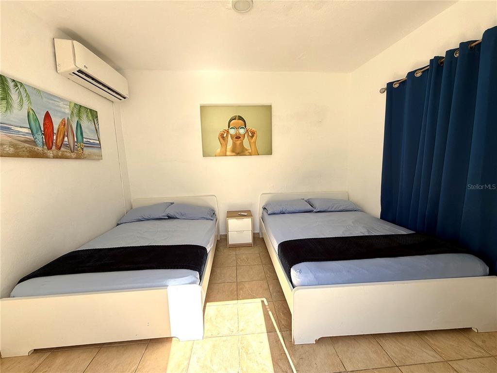 A bedroom features two beds with blue bedding, a small nightstand, and wall-mounted artwork — Carr#3 BEACH FRONT HOUSE AVENUE, PATILLAS, PR