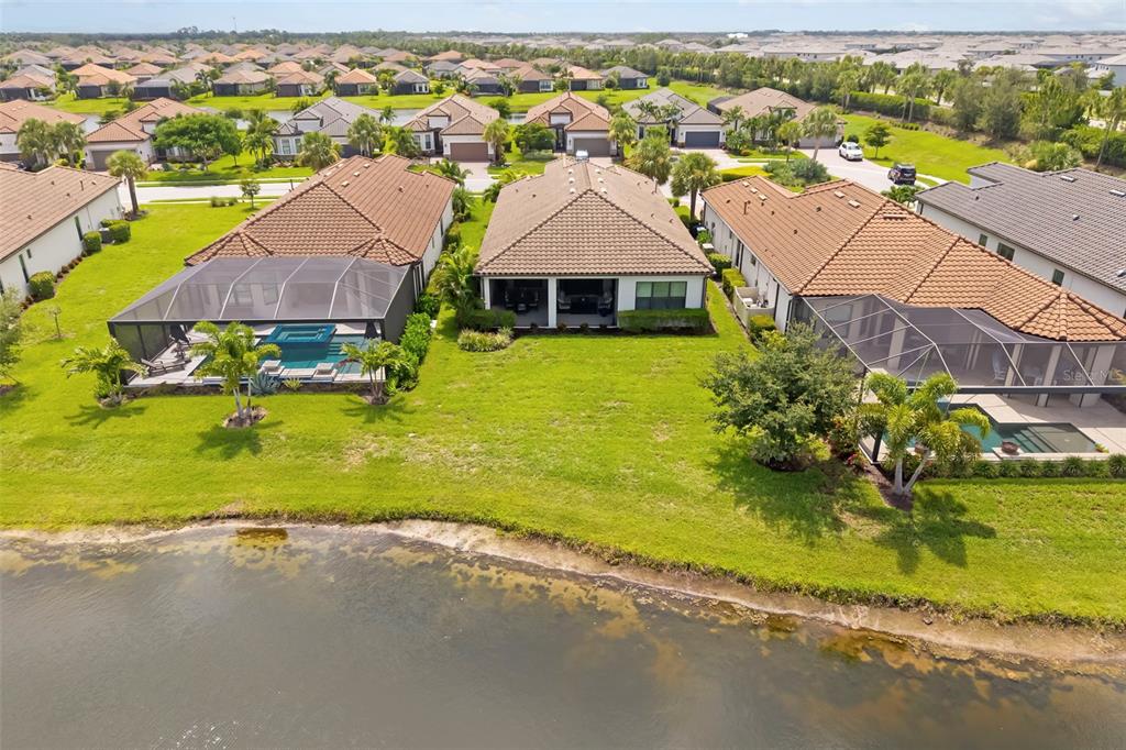 An aerial view shows three houses with tiled roofs, two with screened-in pools, near a lake — 4730 SARCA COURT, BRADENTON, FL