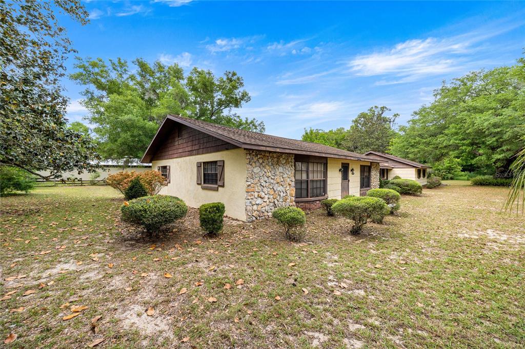 A single-story house with a stone facade, brown siding, and a yard with scattered bushes — 12882 SE 78TH TERRACE, SUMMERFIELD, FL