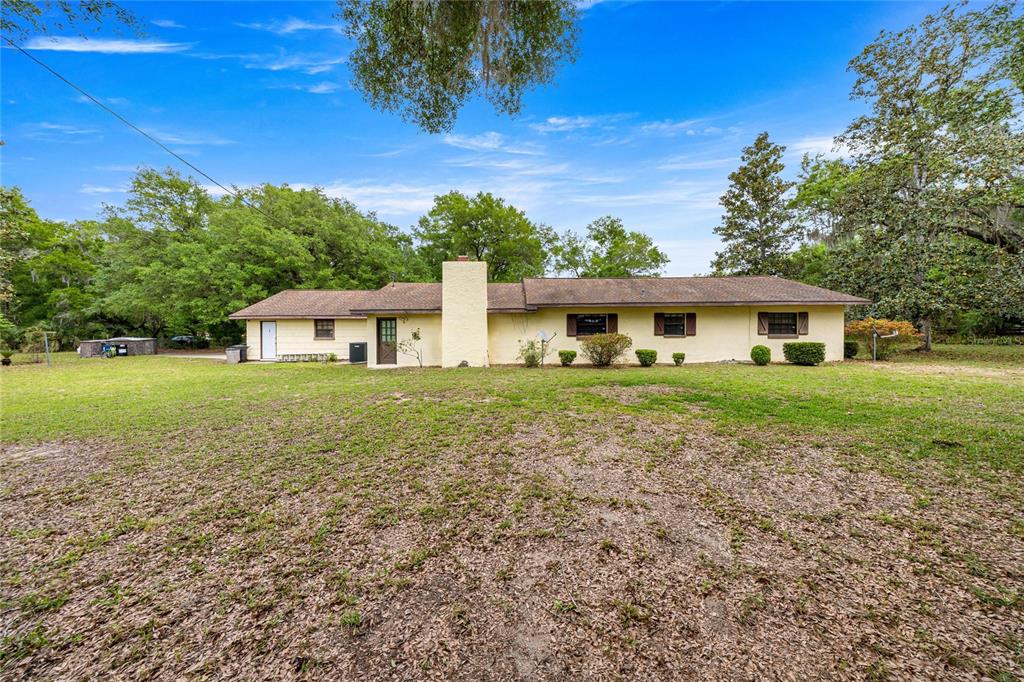 A single-story house with a light-colored exterior and a central chimney sits on a lawn — 12882 SE 78TH TERRACE, SUMMERFIELD, FL