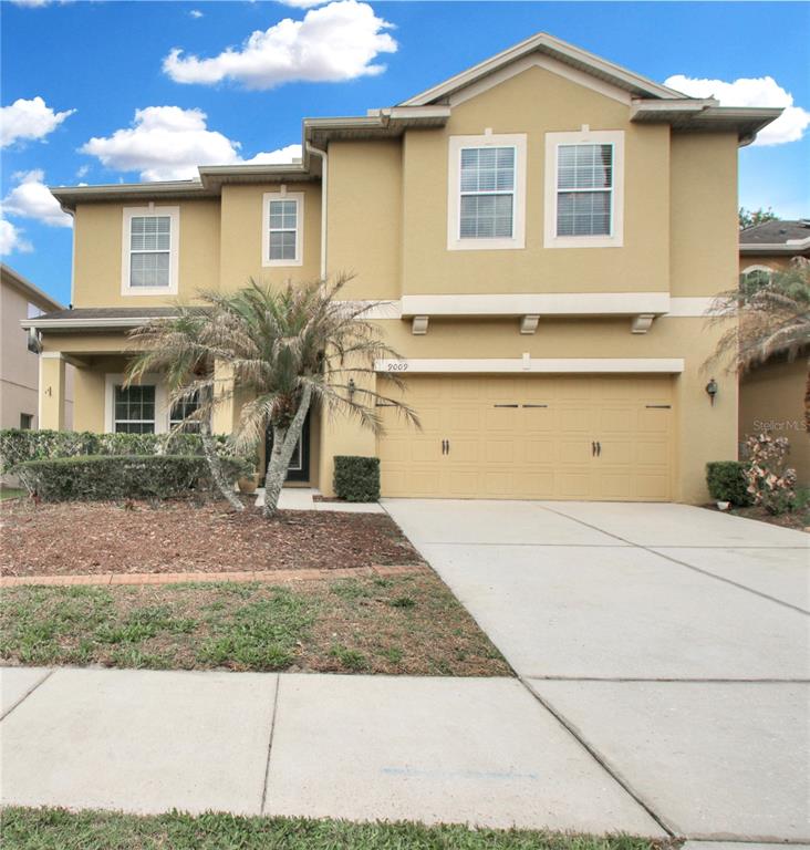 A two-story tan stucco house features a two-car garage and a small front palm tree — 9009 VICKROY TERRACE, OVIEDO, FL