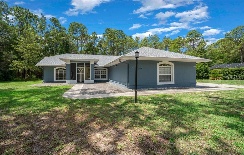 A single-story house with gray stucco siding, a shingled roof, and a paved front patio — 1694 W PEARSON STREET, HERNANDO, FL