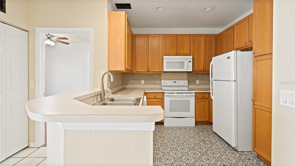 A kitchen with wood cabinets, white appliances, a breakfast bar, and patterned tile flooring — 2586 GRAND CENTRAL PARKWAY UNIT 3, ORLANDO, FL